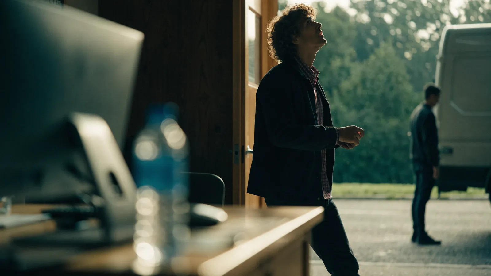 Photo of a pest-control owner pausing in an office doorway by a desktop computer, weighing PestPac alternatives, technician working outside