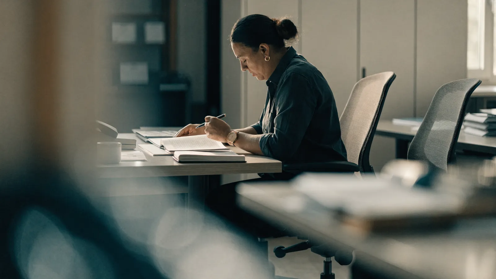 Photo of a pest control office worker focused on paperwork at a desk surrounded by empty chairs, illustrating administrative labor that scales with headcount.