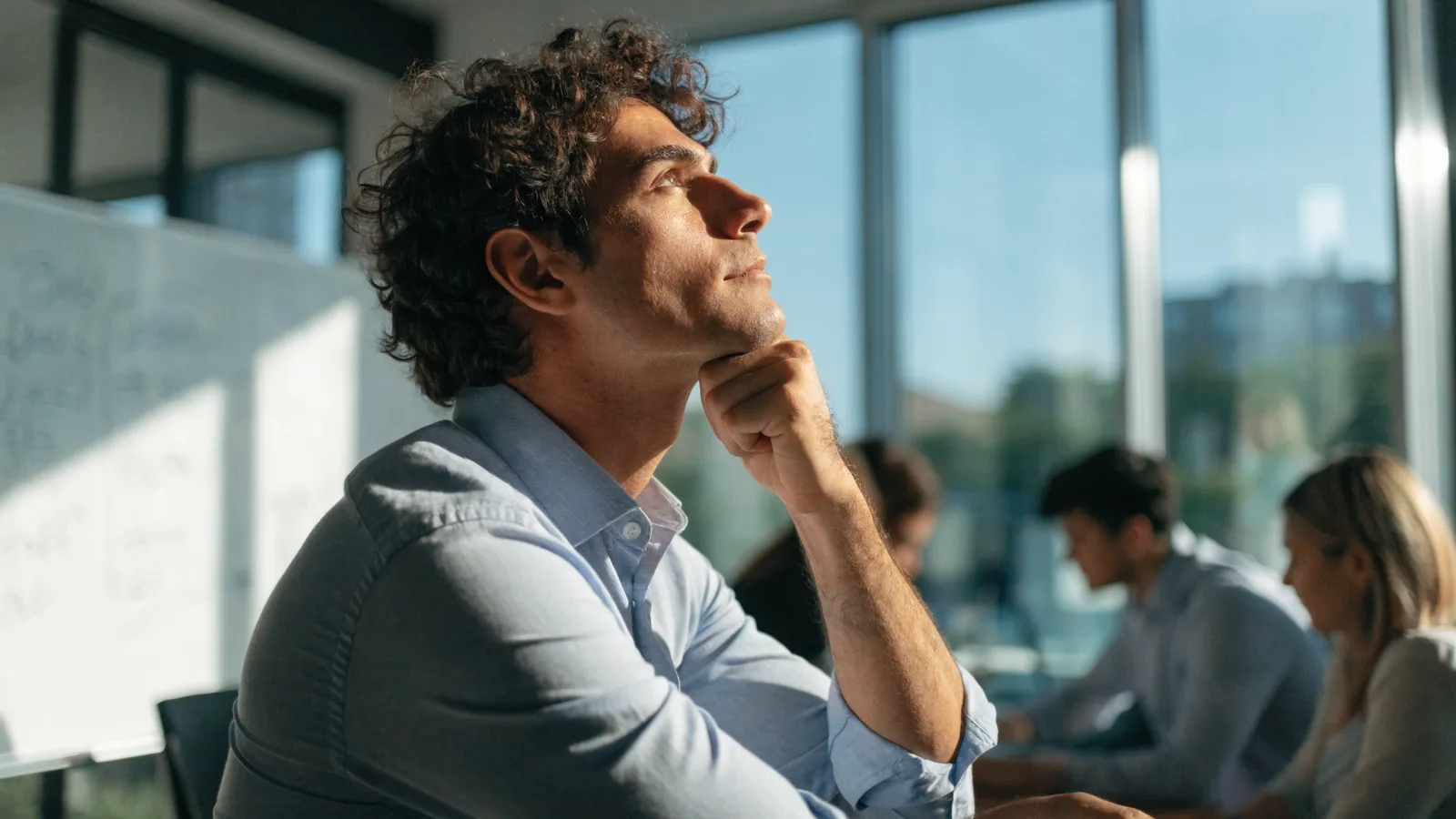 Color photo of a pest-control business owner at a bright whiteboard wall weighing two software paths, colleagues blurred behind in vivid daylight.